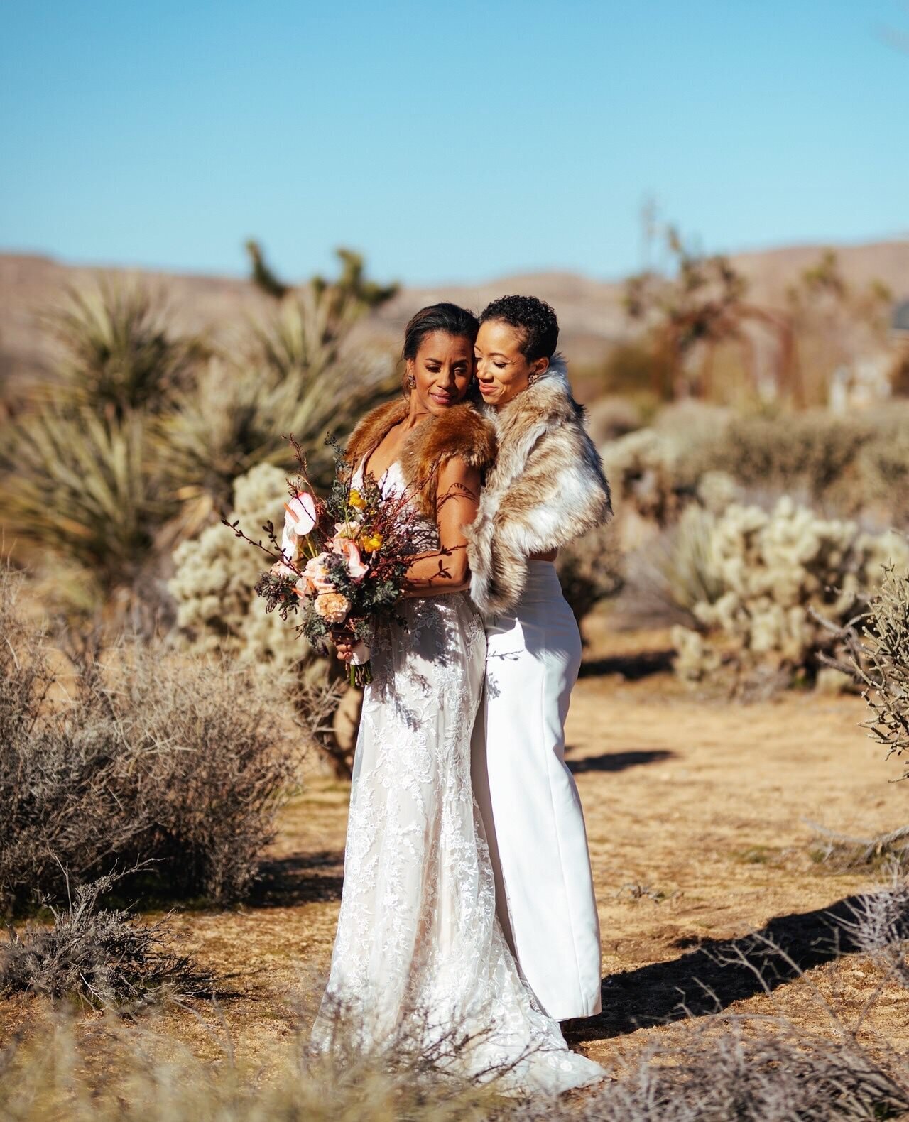 Two brides in white and fur posing together in the Palm Springs desert Shawnee Custalow Queer Wedding Photographer