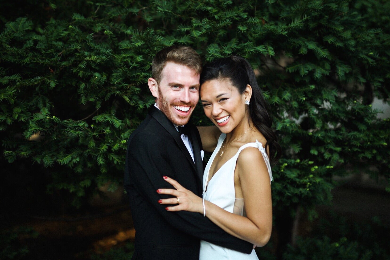 Bride and groom smiling and posing together by a green hedge in Richmond VA Shawnee Custalow Queer Wedding Photographer