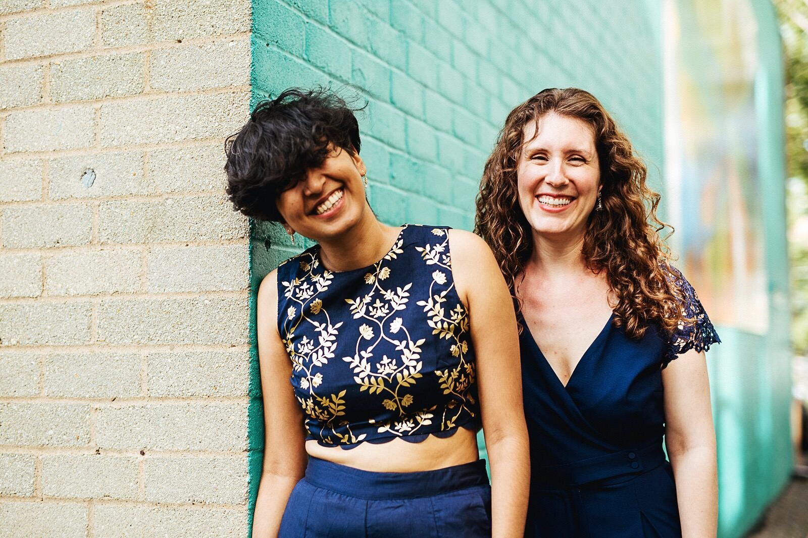 LGBTQ couple posing together by a turquoise brick wall Richmond VA Shawnee Custalow Queer Wedding Photographer