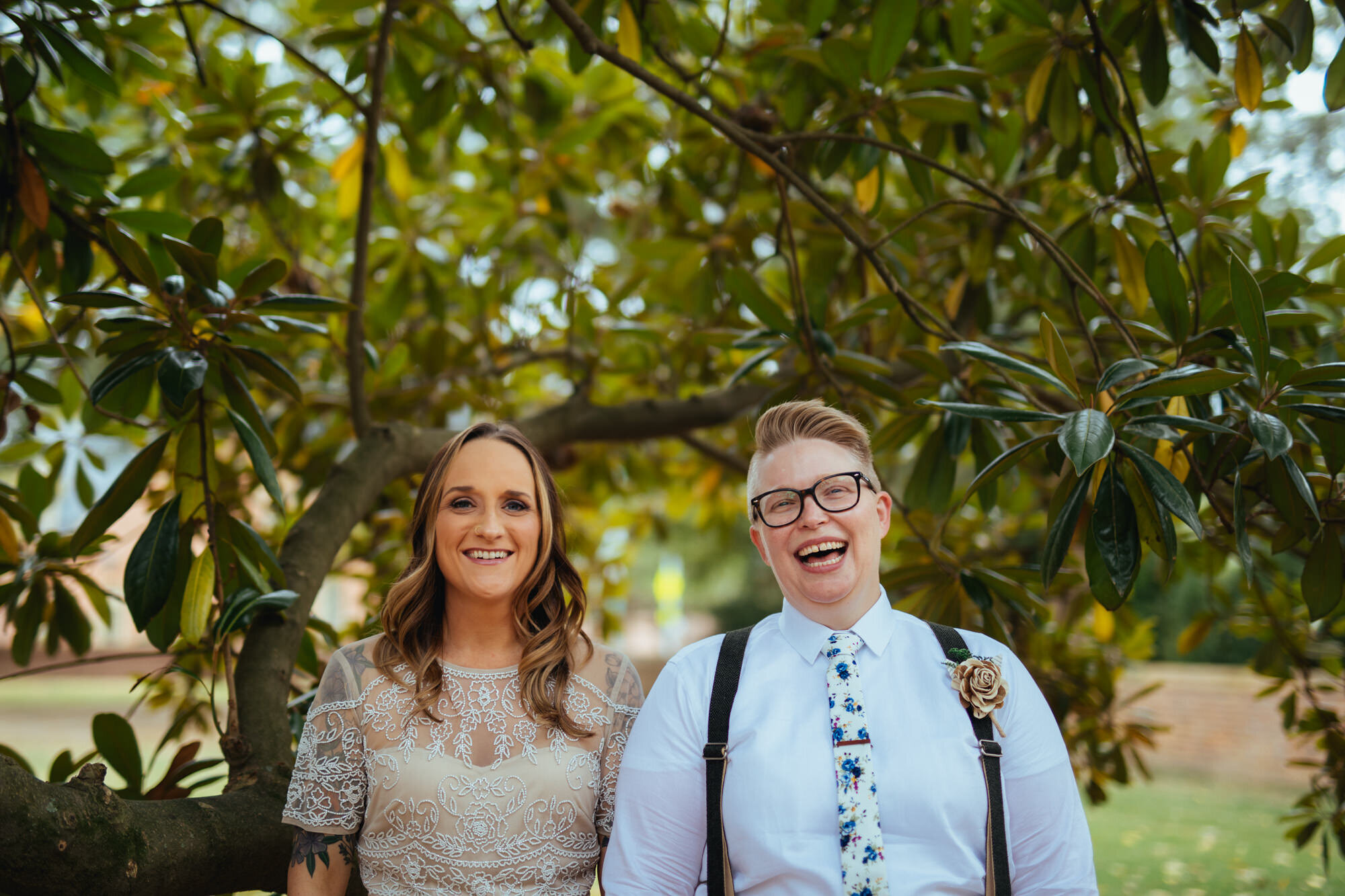 Newlywed LGBTQ couple smiling under a magnolia tree in Richmond VA Shawnee Custalow Queer Wedding Photographer