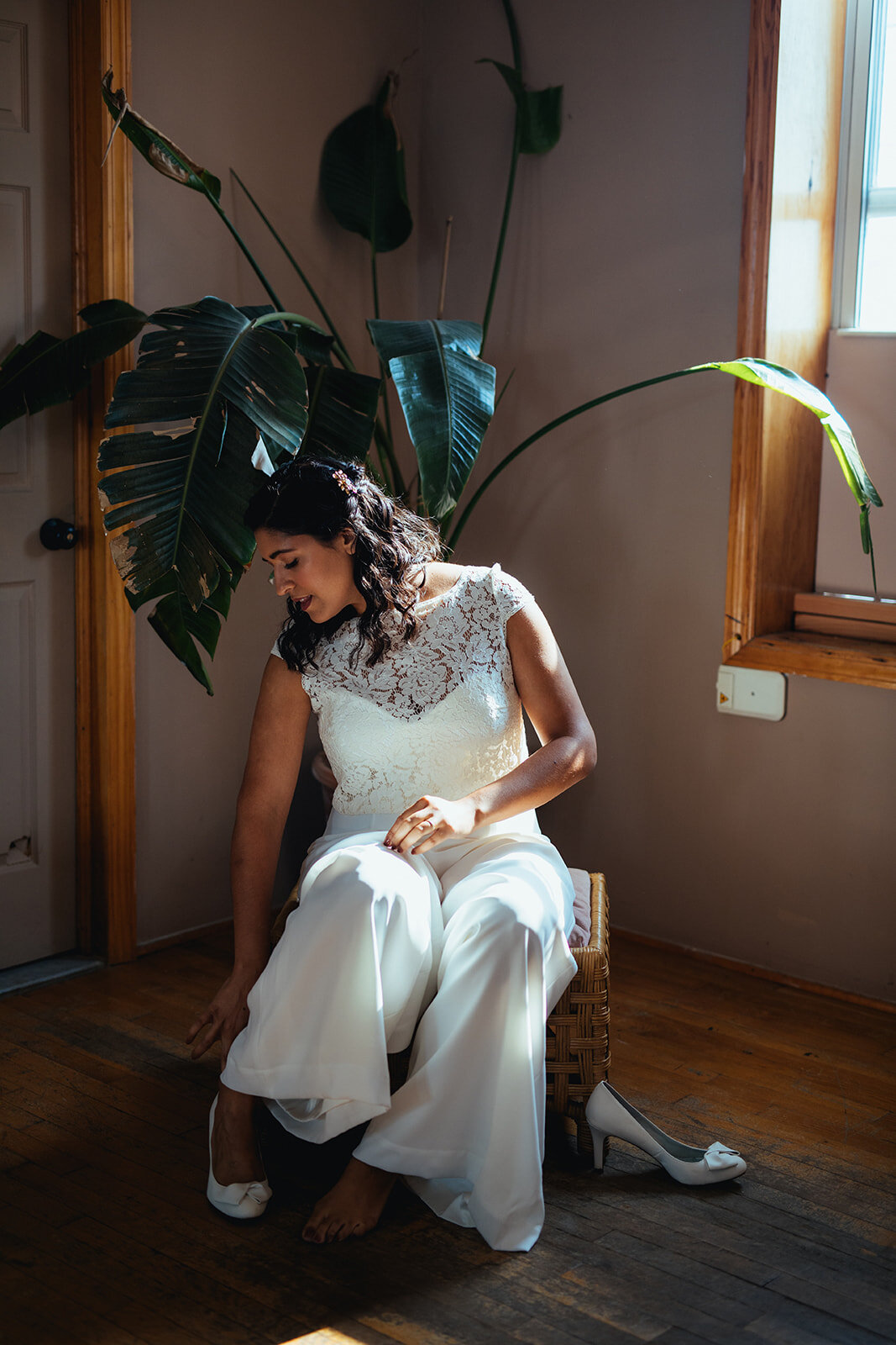 Bride in white jumpsuit putting her heels on in Red Hook Brooklyn Shawnee Custalow Queer Wedding Photographer