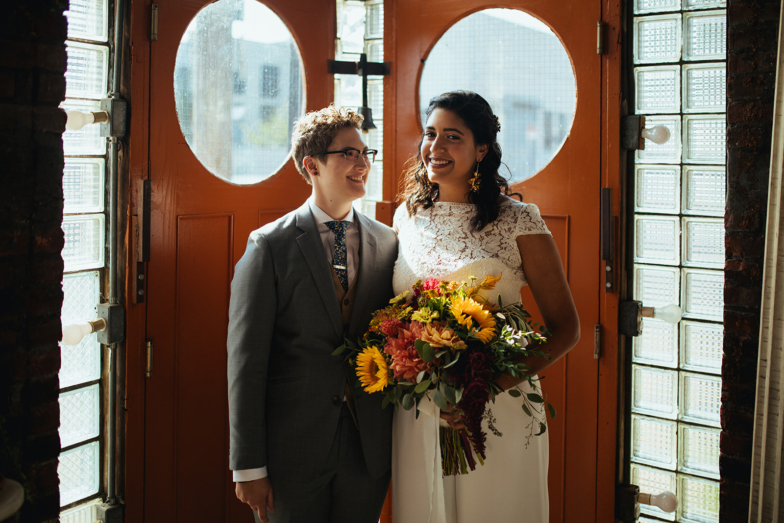 LGBTQ wedding couple posing before orange doors at Marlow Events in Brooklyn Shawnee Custalow Queer Wedding Photographer