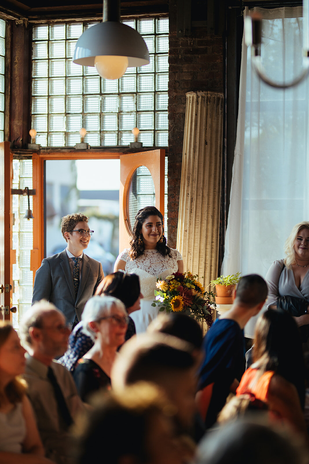 LGBTQ couple watching their wedding guest during the ceremony at Marlow Events Red Hook Brooklyn Shawnee Custalow Queer Wedding Photographer