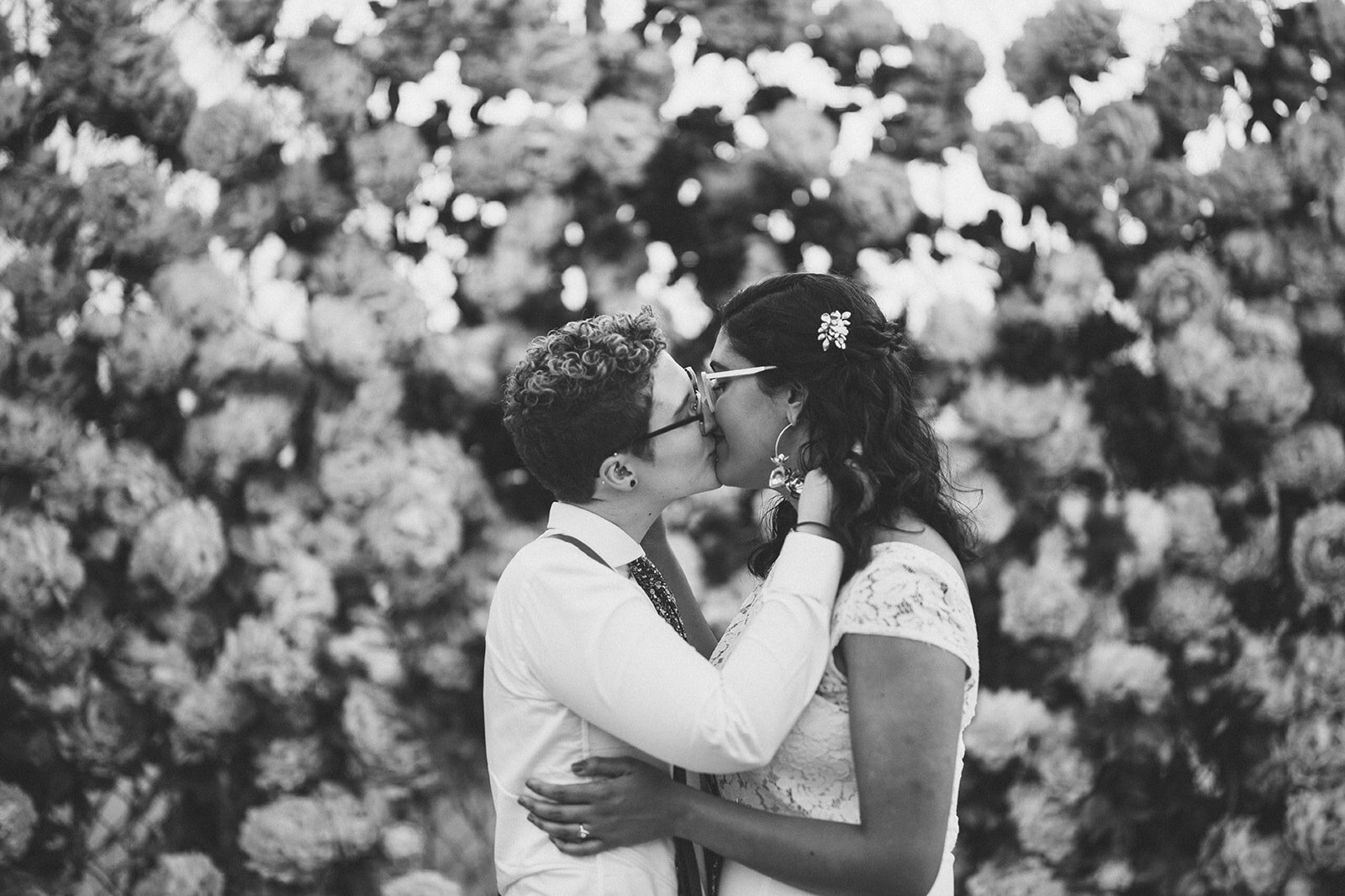 LGBTQ newlywed couple kissing by big flowers in Red Hook Brooklyn Shawnee Custalow Queer Wedding Photographer