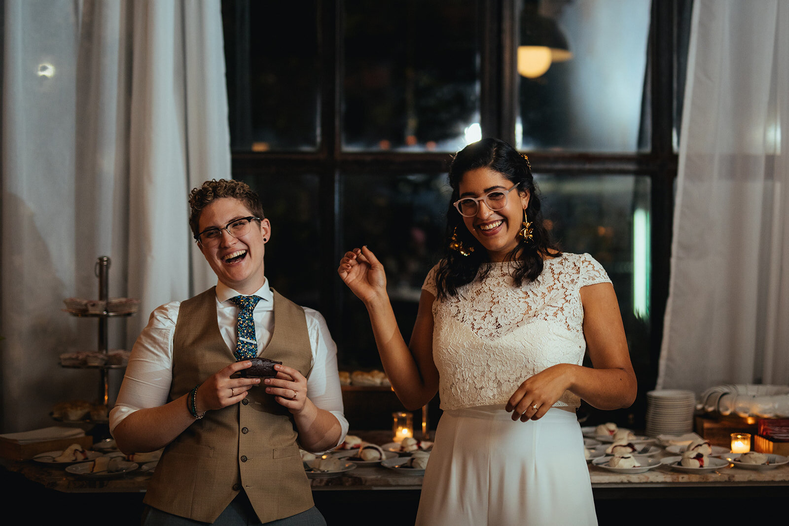 Newlywed lgbtq couple laughing before eating cake at Marlow Events Red Hook Brooklyn Shawnee Custalow Queer Wedding Photographer