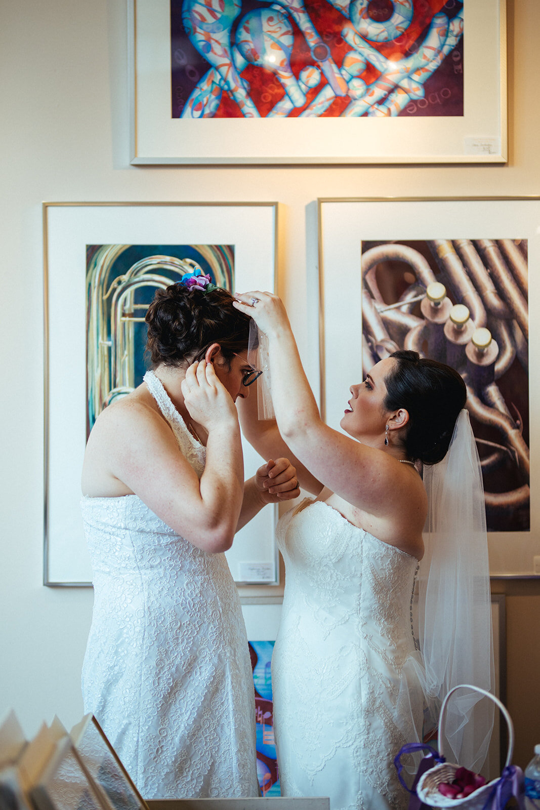 Two brides helping each other get ready at Torpedo Factory Alexandria VA Shawnee Custalow Queer Wedding Photography