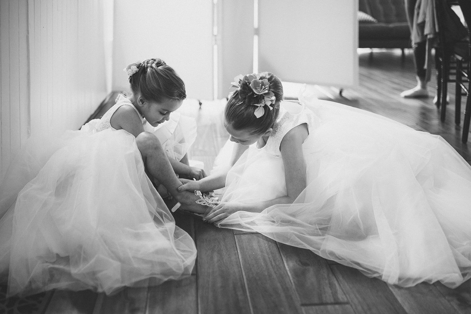 Two little girls helping each other put shoes on in Alexandria VA Shawnee Custalow Queer Wedding Photography