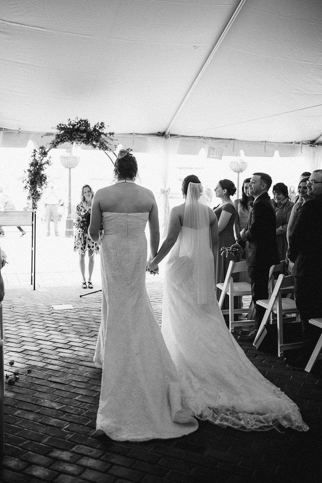 Two brides holding hands walking down the aisle at Torpedo Factory Alexandria VA Shawnee Custalow