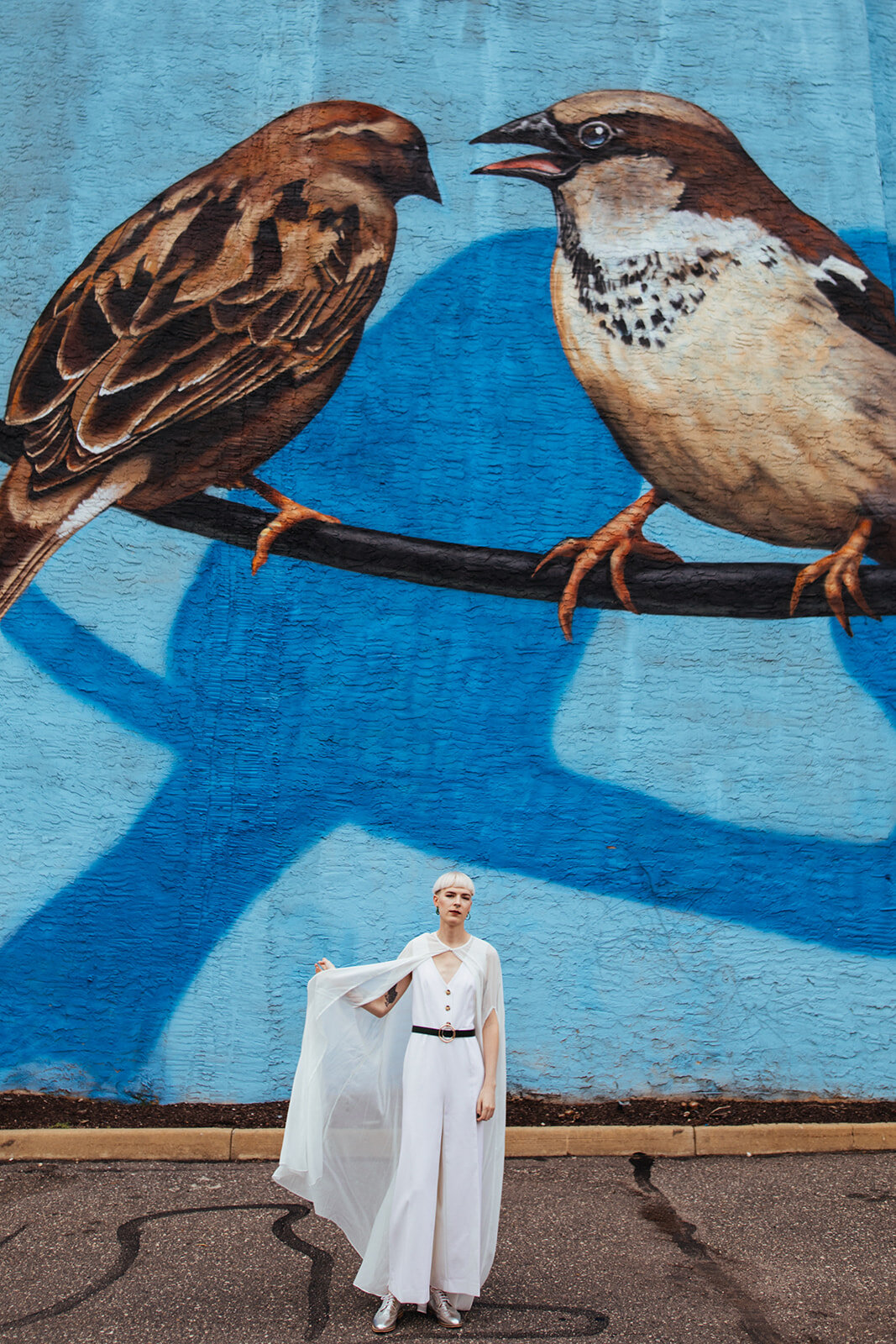 Future spouse with cape by a bird mural in Philly PA Shawnee Custalow Queer Wedding Photography