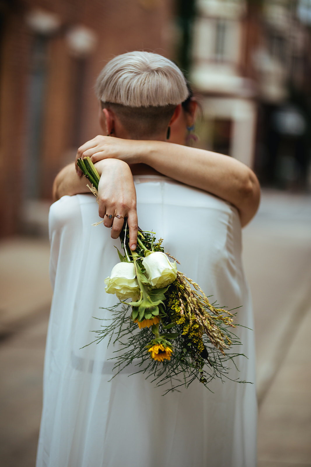 Future spouses embracing while holding bouquet in Philly Shawnee Custalow Queer Wedding Photography