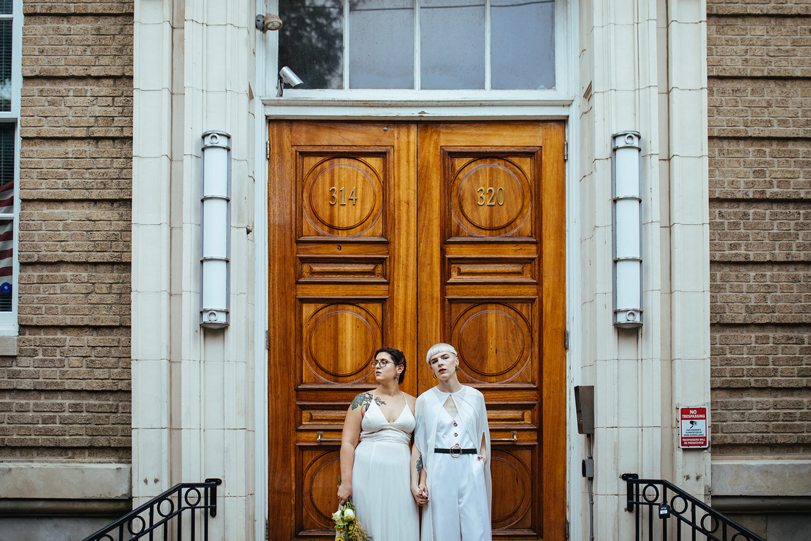 Newlyweds holding hands outside wooden doors in Philly PA Shawnee Custalow Queer Wedding Photography