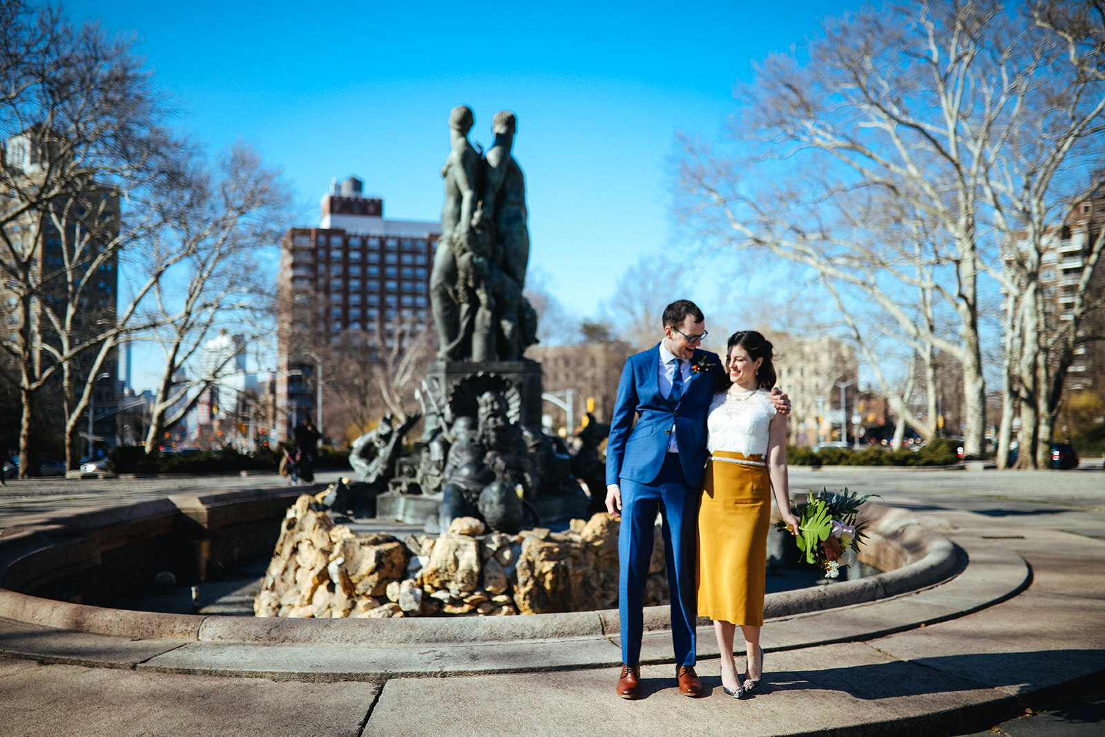 Bride and groom embracing by a monument in NYC Shawnee Custalow queer wedding photography