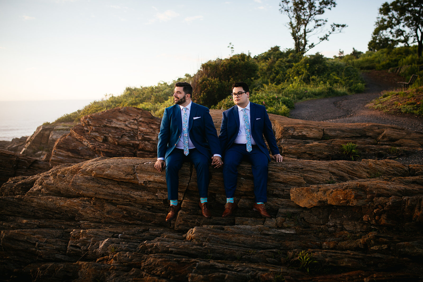 Future spouses holding hands on a rock on Peaks Island Portland ME Shawnee Custalow Queer wedding photography