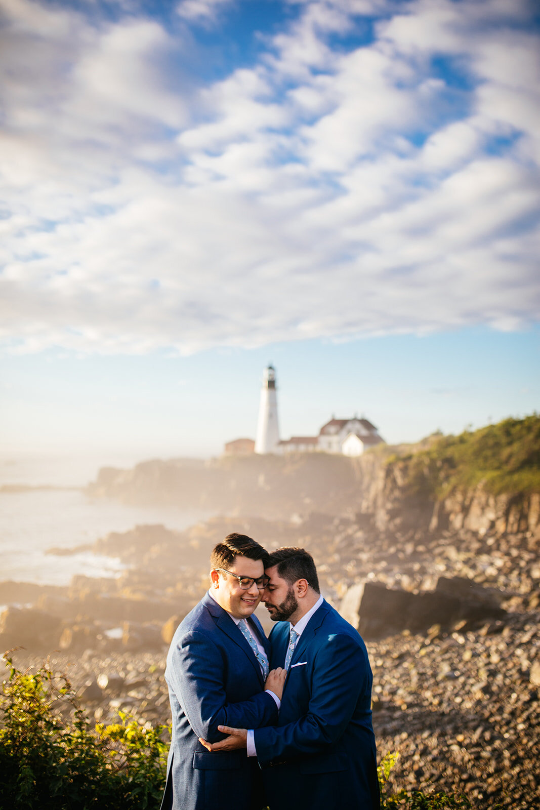 LGBTQ couple embracing under light house on Peaks Island Portland ME Shawnee Custalow Queer wedding photography