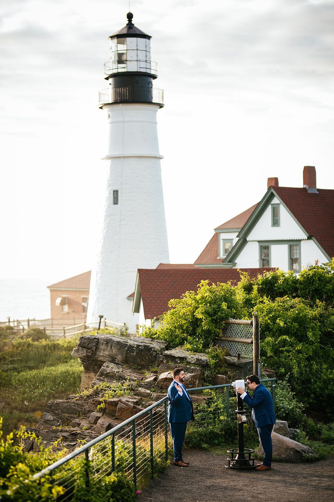 LGBTQ couple using binoculars under light house on Peaks Island Portland ME Shawnee Custalow wedding photography