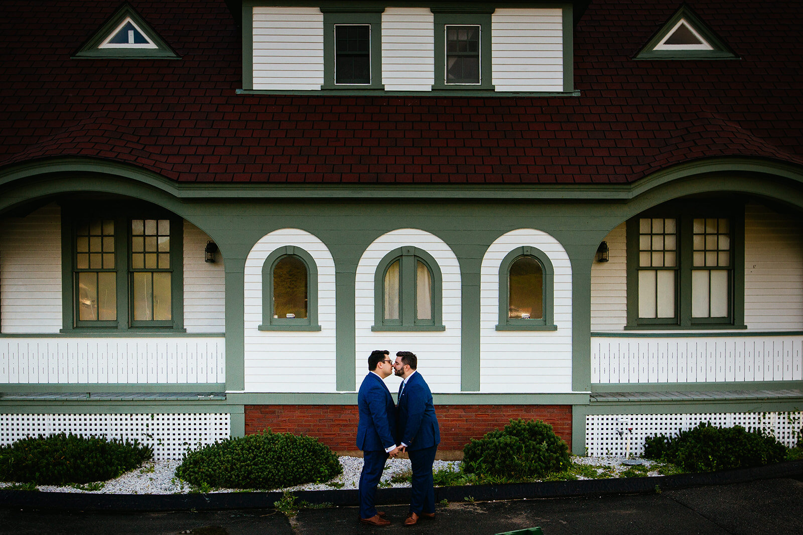 Grooms leaning in for a kiss by a green and white house on Peaks Island Portland ME Shawnee Custalow wedding photography
