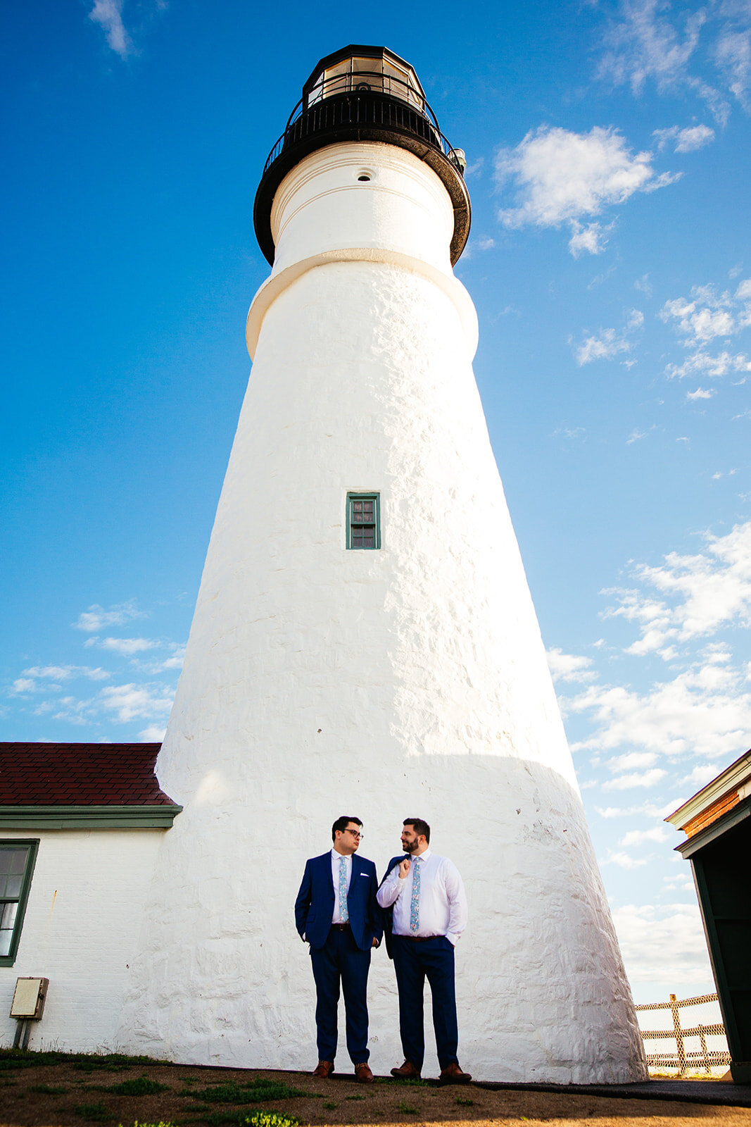 LGBTQ grooms standing under a light house on Peaks Island Portland ME Shawnee Custalow Queer wedding photography