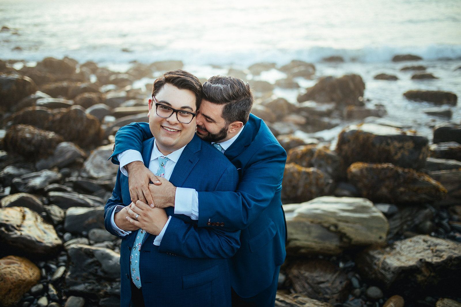Queer couple embracing on a rocky beach in Peaks Island Portland ME Shawnee Custalow wedding photography