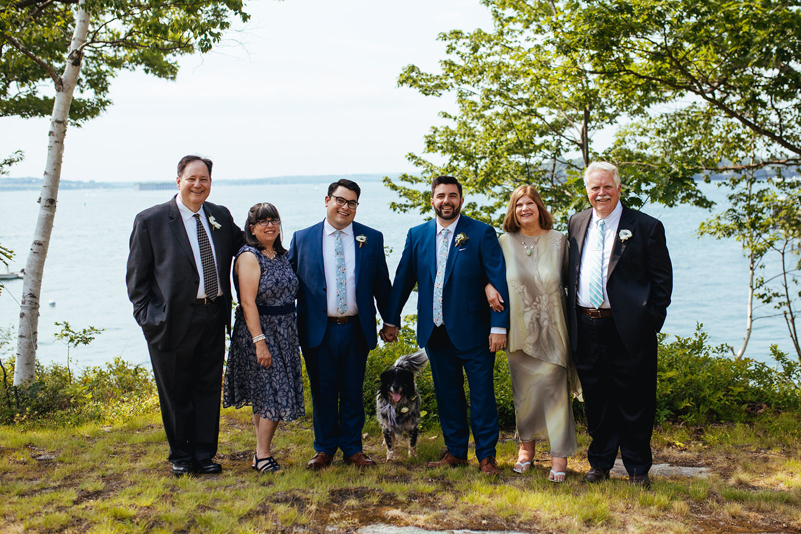 Grooms posing with family and dog on Peaks Island Portland ME Shawnee Custalow Queer wedding photography