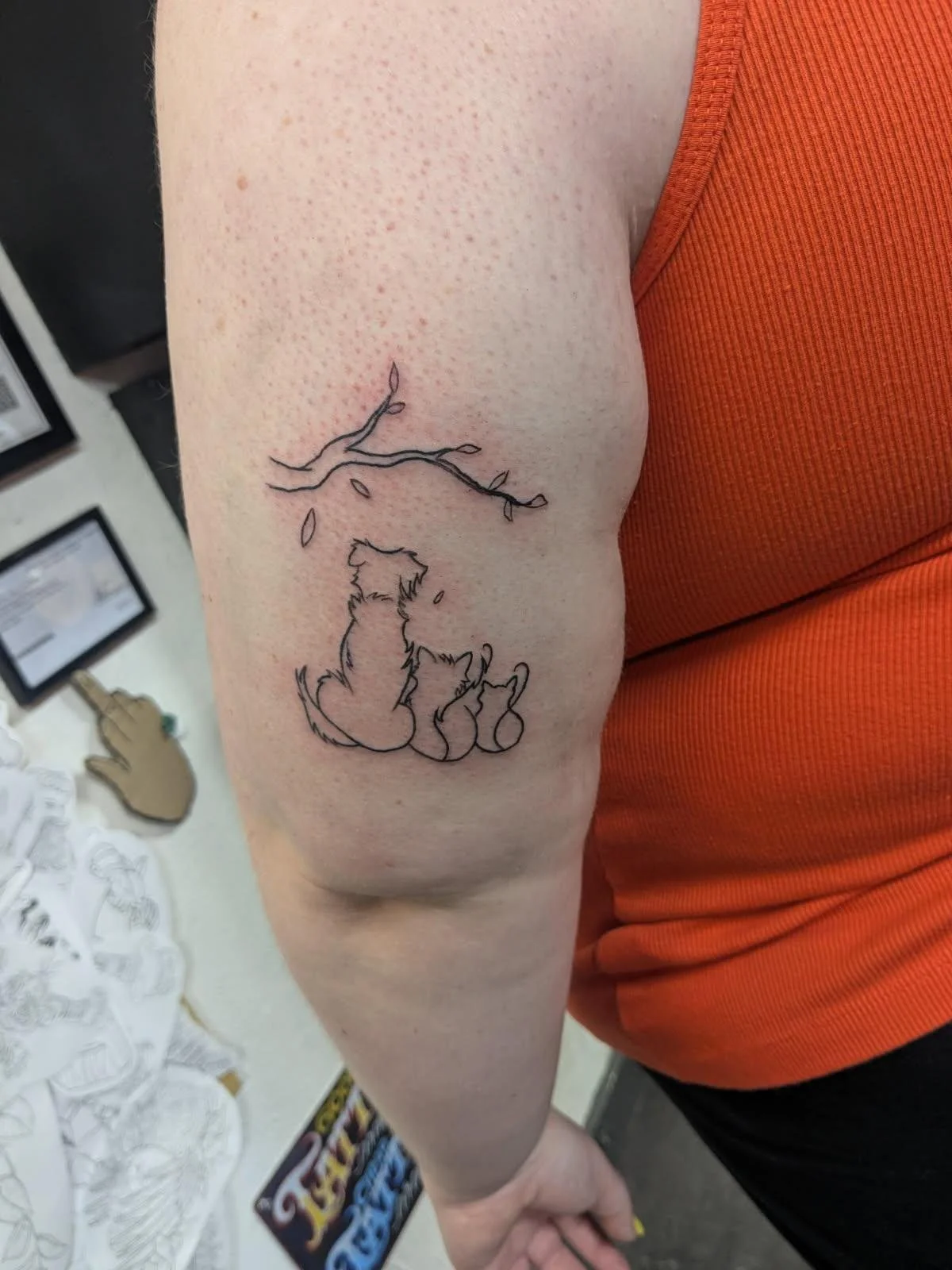 Tattoo of three dogs sitting under a tree branch on a person's upper arm.