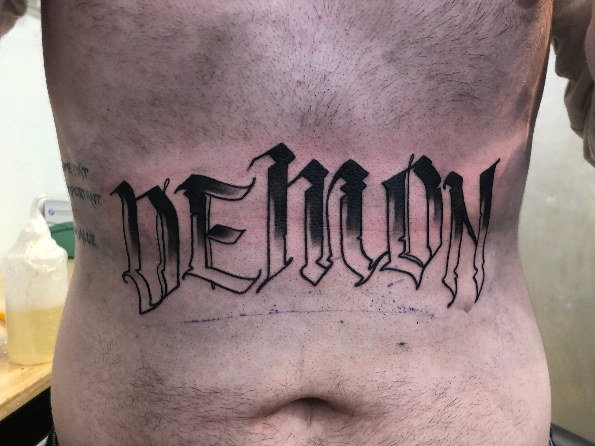 Gothic-style tattoo reading 'DEMON' on lower back