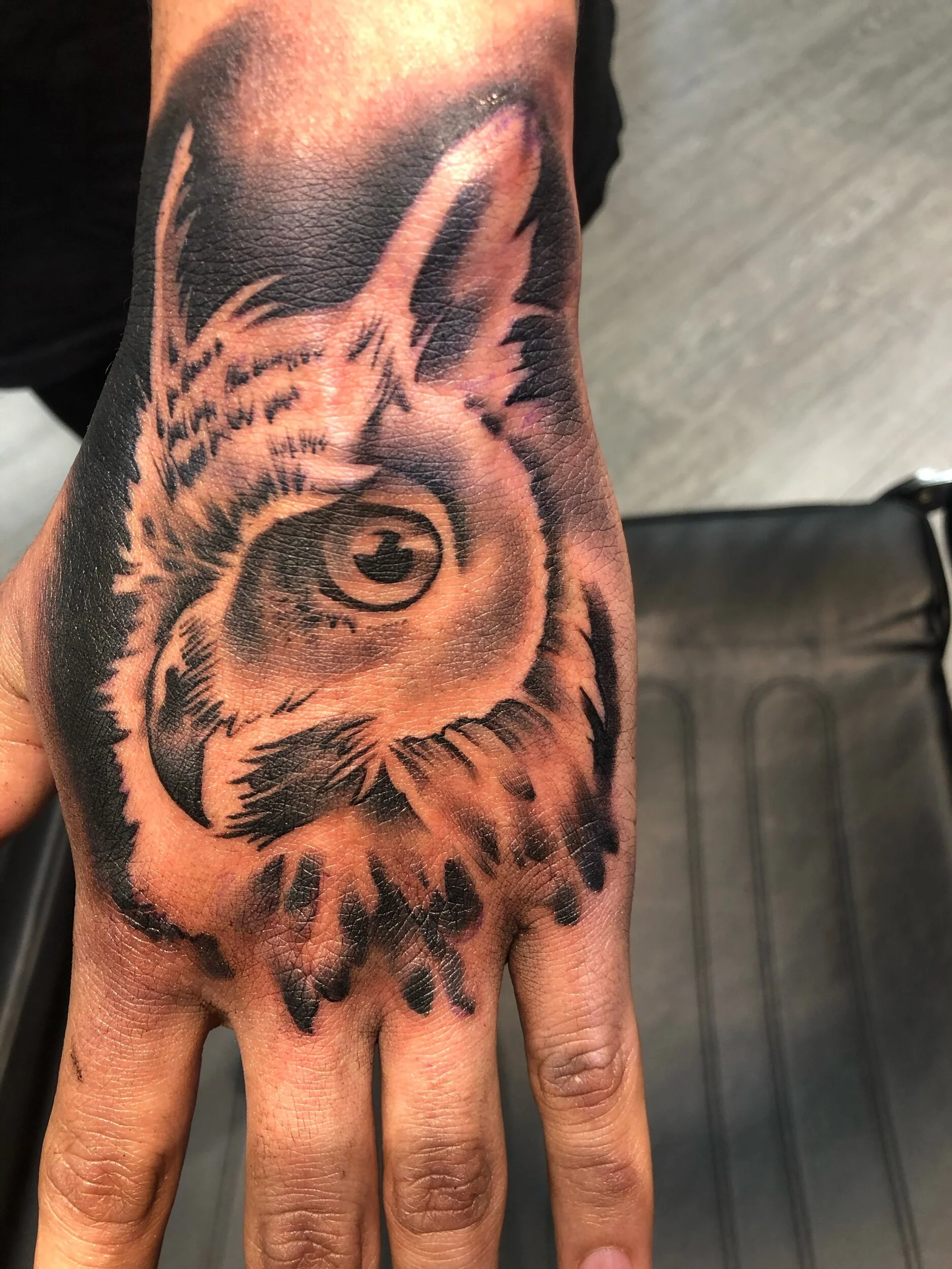 Hand tattoo of an owl's face with intricate shading and detail.