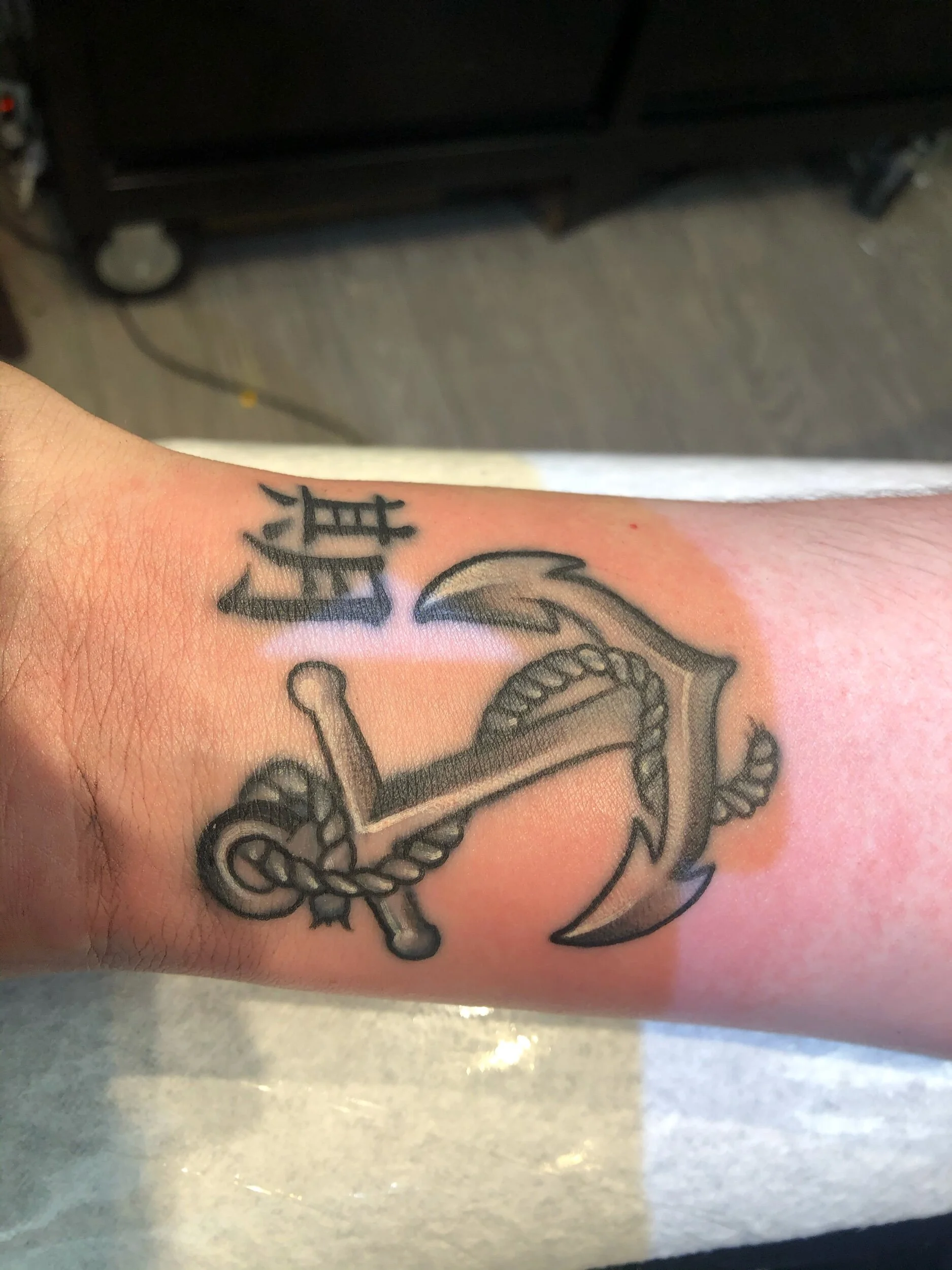Tattoo of an anchor with rope and Chinese characters on a person's forearm.