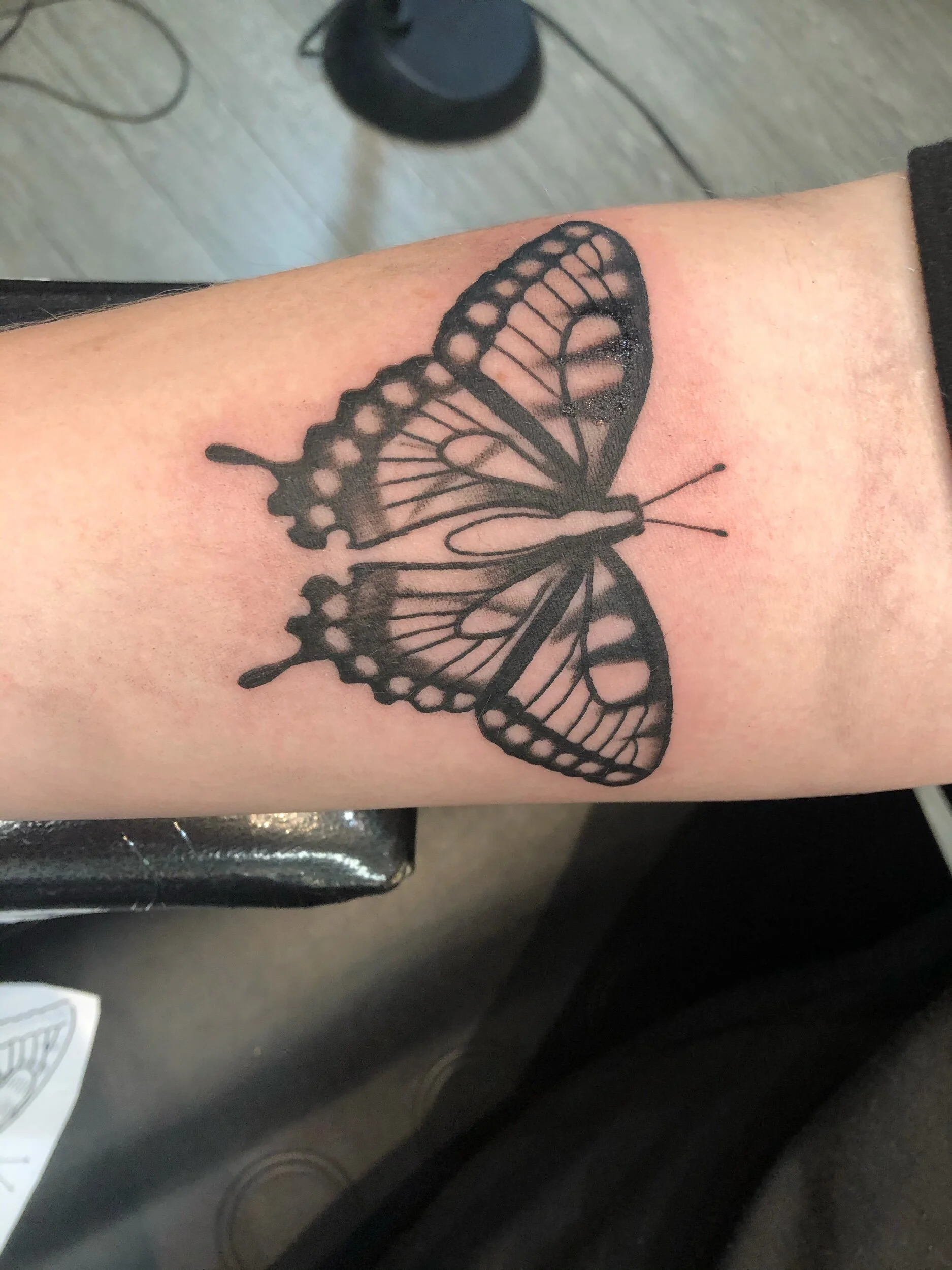 Black butterfly tattoo on forearm