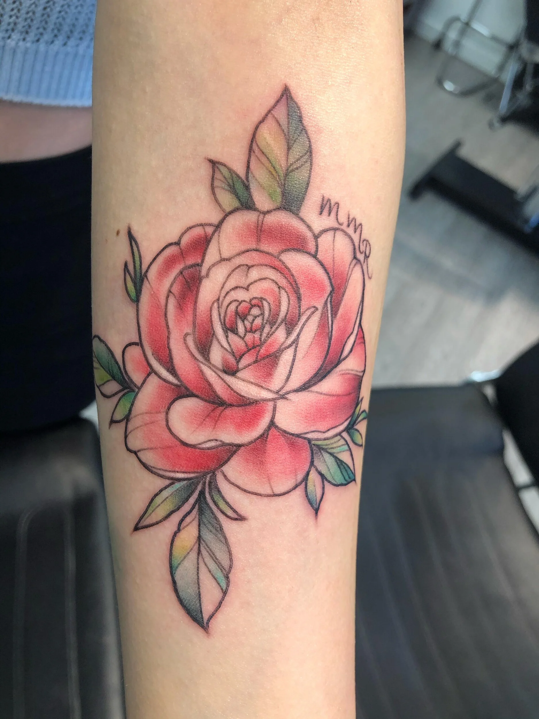 A tattoo of a red and pink rose with green and multi-colored leaves on an arm.