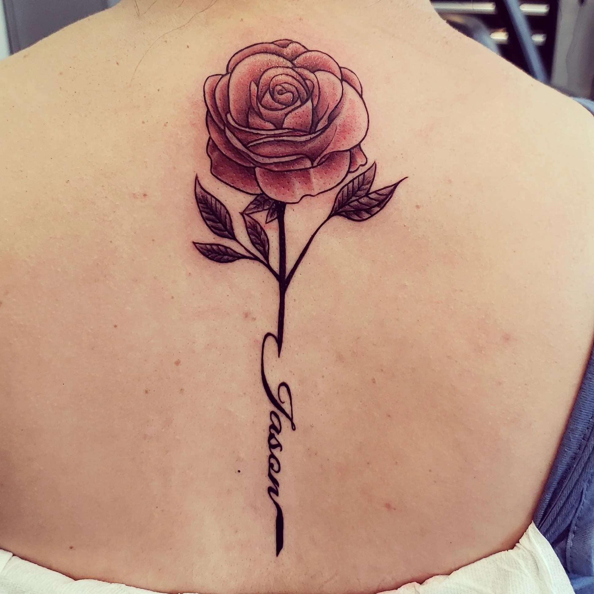 Rose tattoo with text, displayed on a person's back.