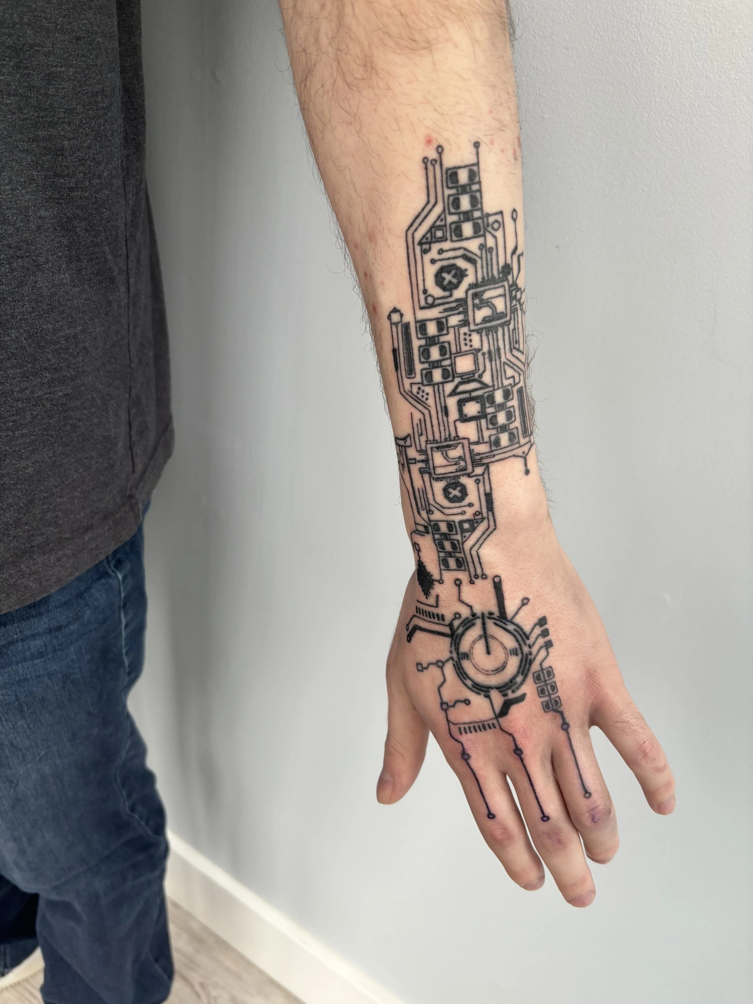 A person's forearm with a tattoo of a circuit board design, extending from the wrist to the elbow.