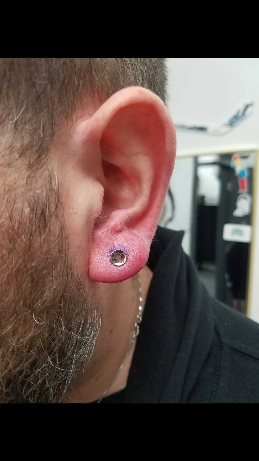 Close-up of a man's ear with a small metal gauge piercing in the earlobe.