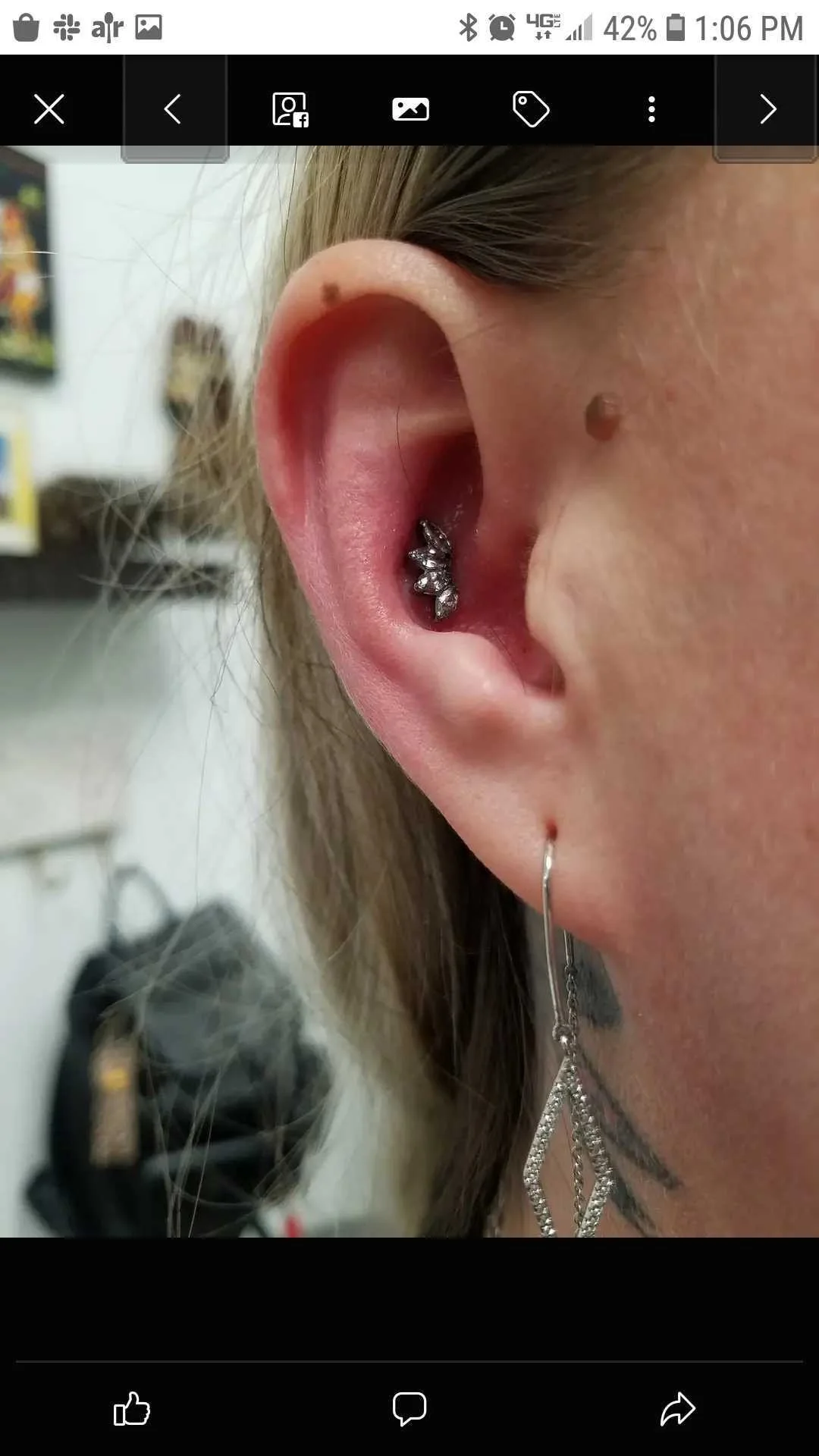 Close-up of an ear with two piercings, one with a small decorative stud and another with a dangling earring.
