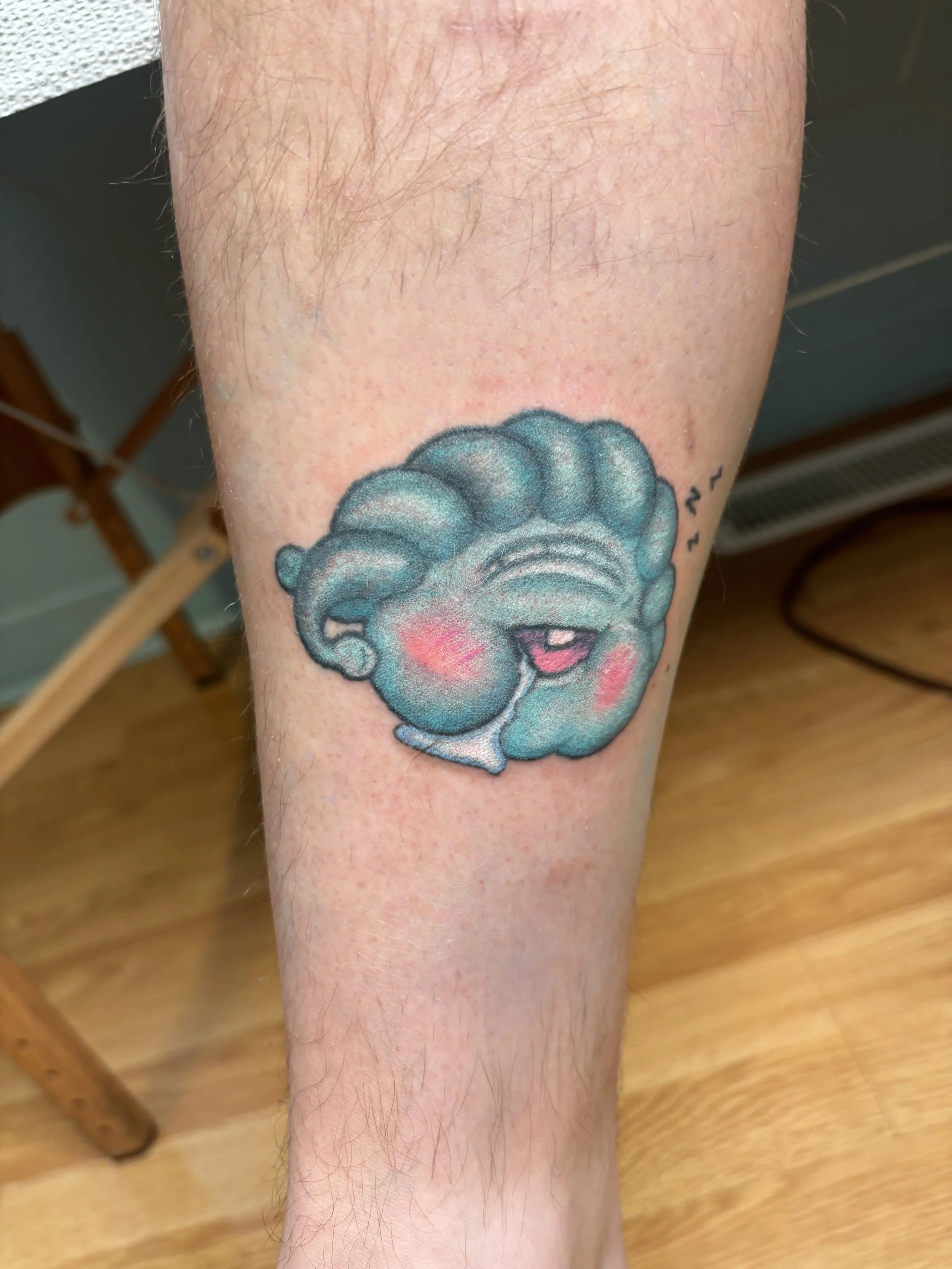 Colorful tattoo of a smiling pony with blue hair, pink cheeks, and a pink tongue, on a person's calf.