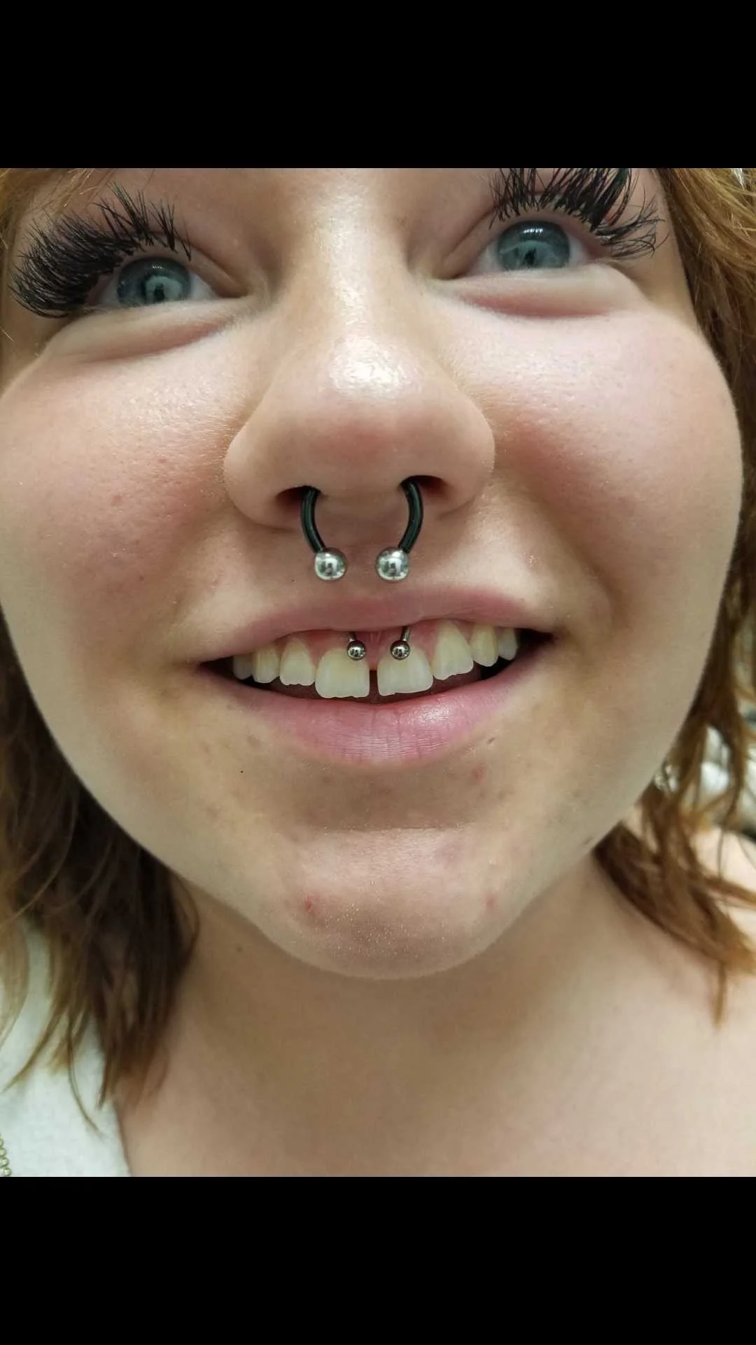 Close-up of a person with a septum piercing and a smiley piercing, showing eyelashes.
