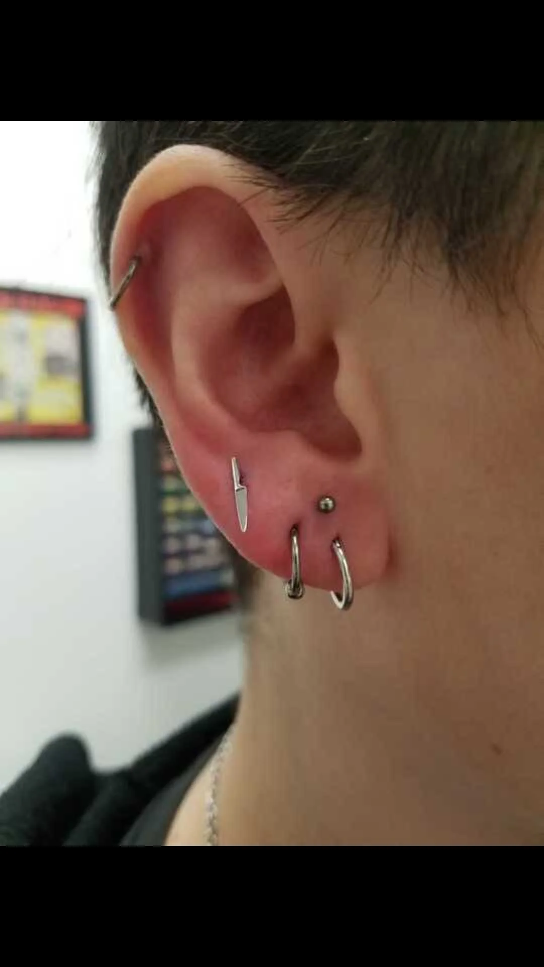 Ear with multiple piercings, including hoop and barbell earrings, and a knife-shaped stud.