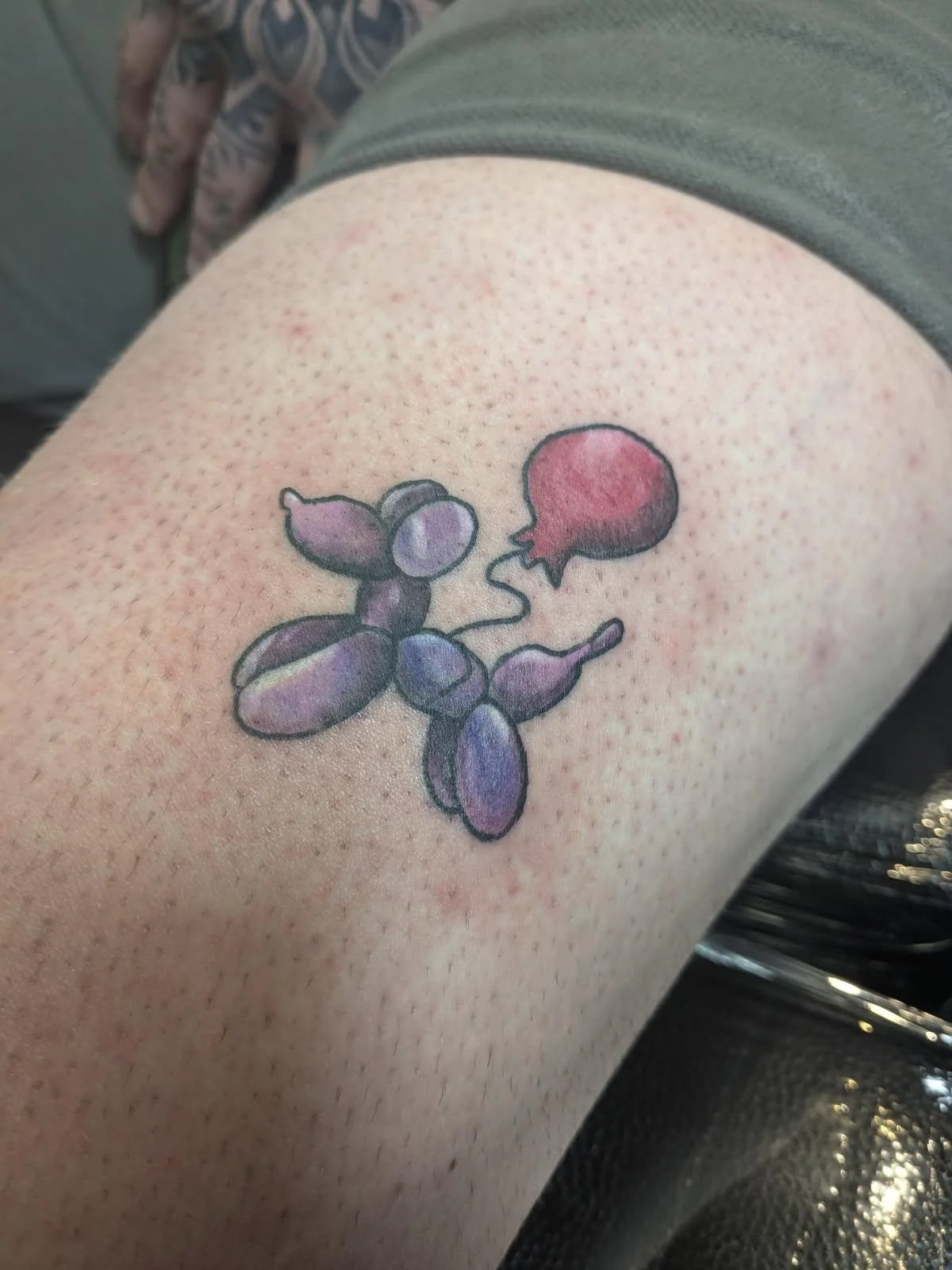 Tattoo of purple balloon animals holding a red balloon on person's upper thigh.