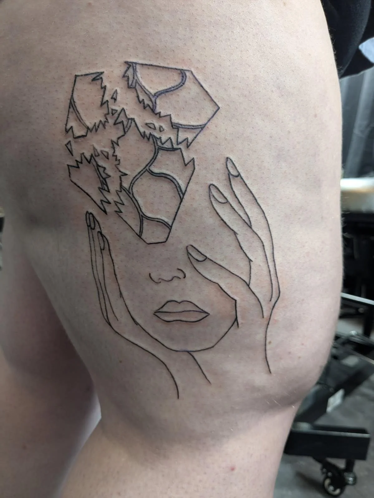 Tattoo of a woman's face with her eyes closed, surrounded by her hand and a mountainous landscape with trees.