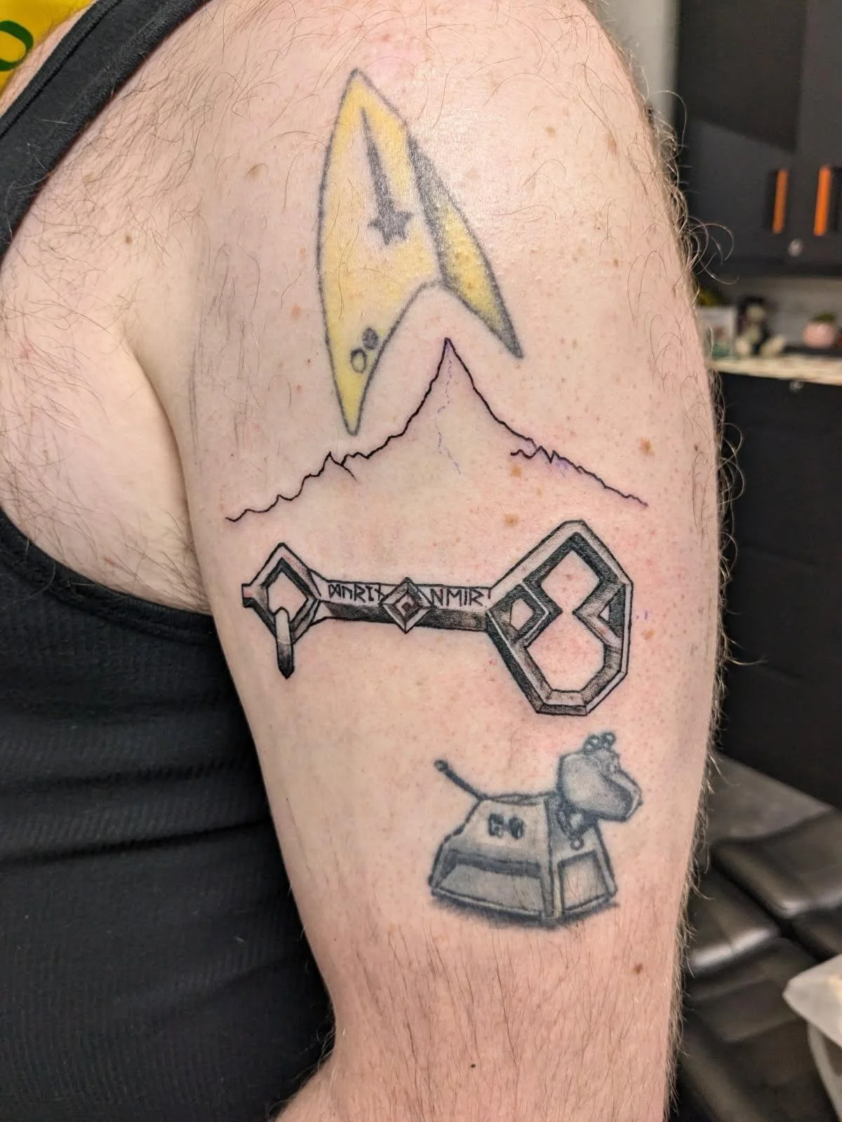 Tattoo of a spaceship, mountain range, key, and a cartoon mouse wearing headphones on a person's upper arm.