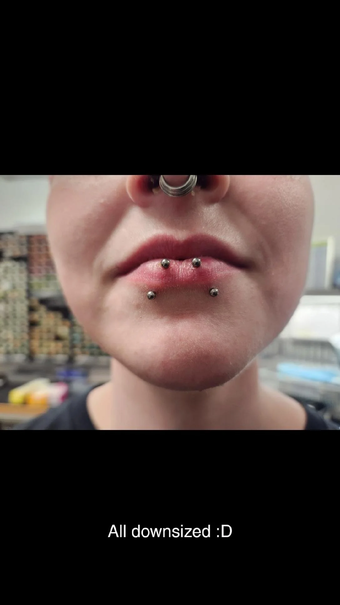 Close-up of a person's lips with multiple lip piercings and a septum ring.