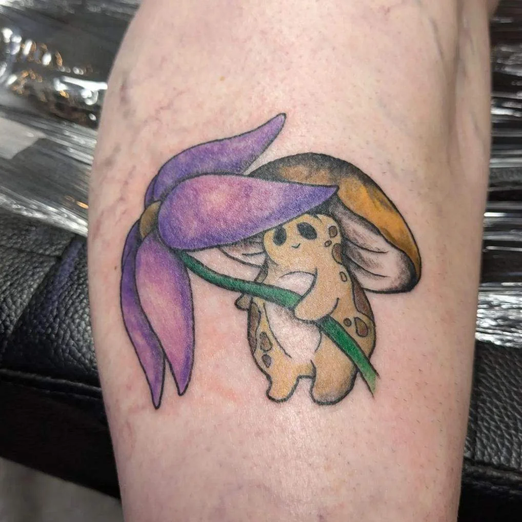 Colorful tattoo of a cute baby cheetah with large eyes holding a purple flower with green stem and leaves.