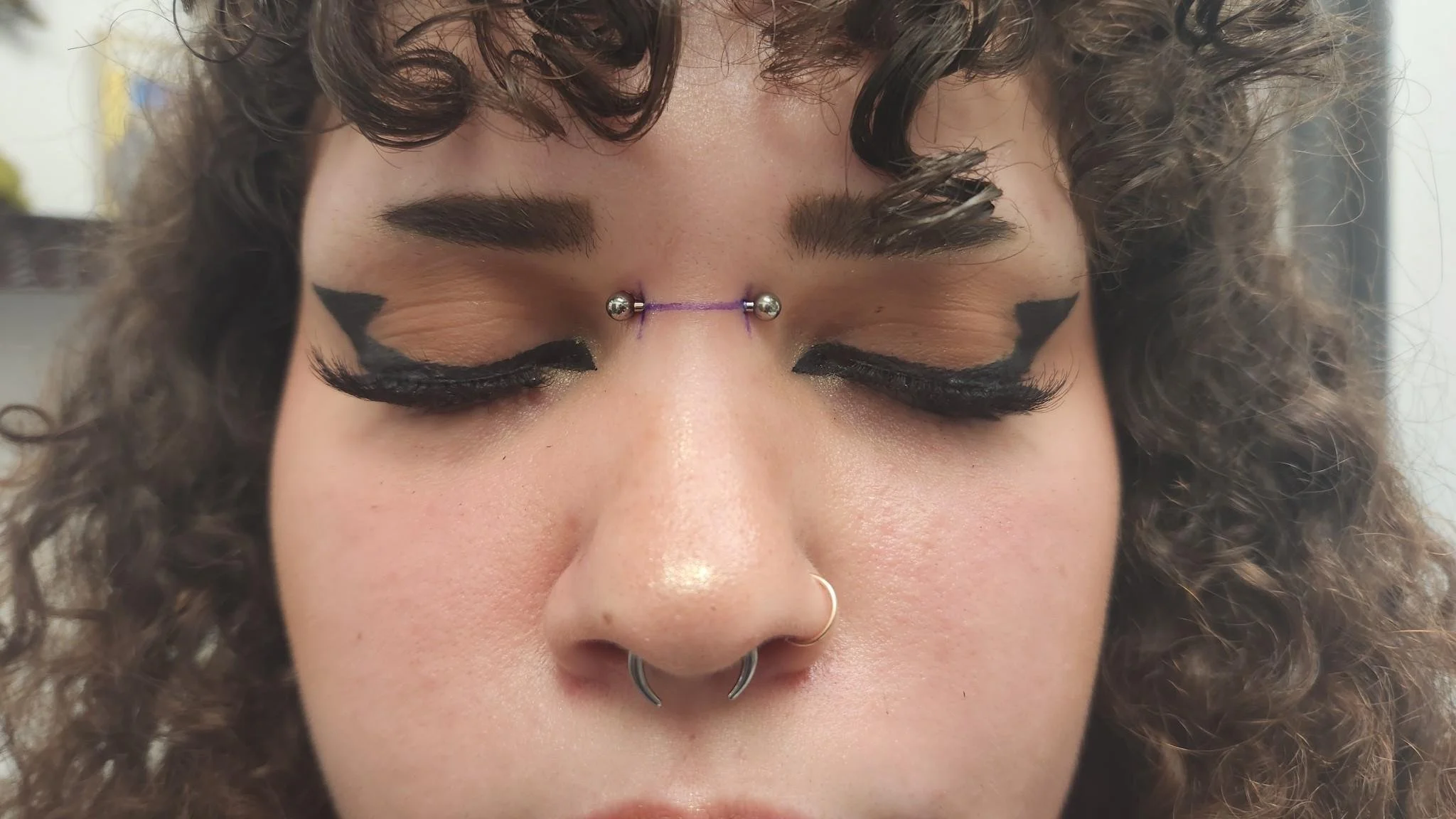 Person with eyebrow piercing, bold eye makeup, and septum ring