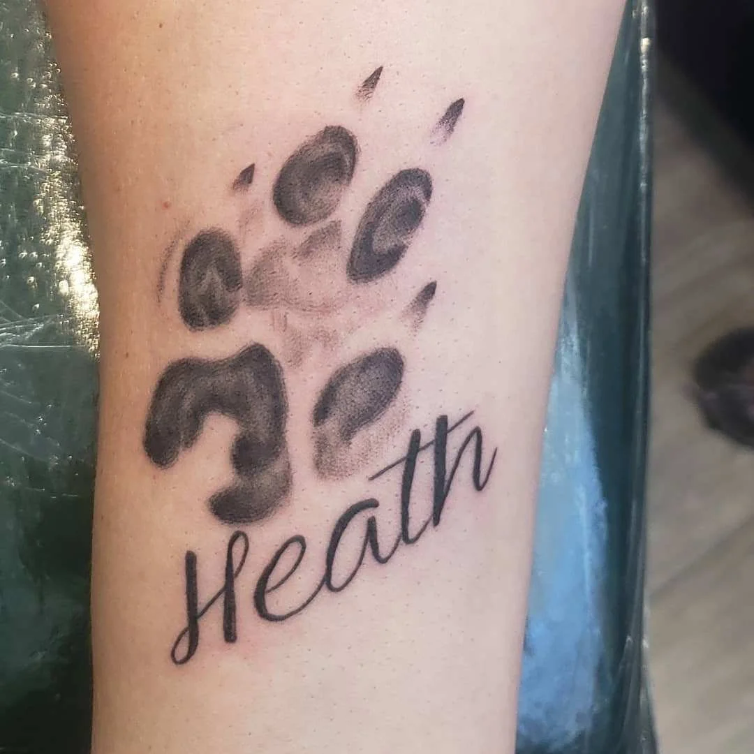 Tattoo of a shaded paw print with the name "Heath" underneath.