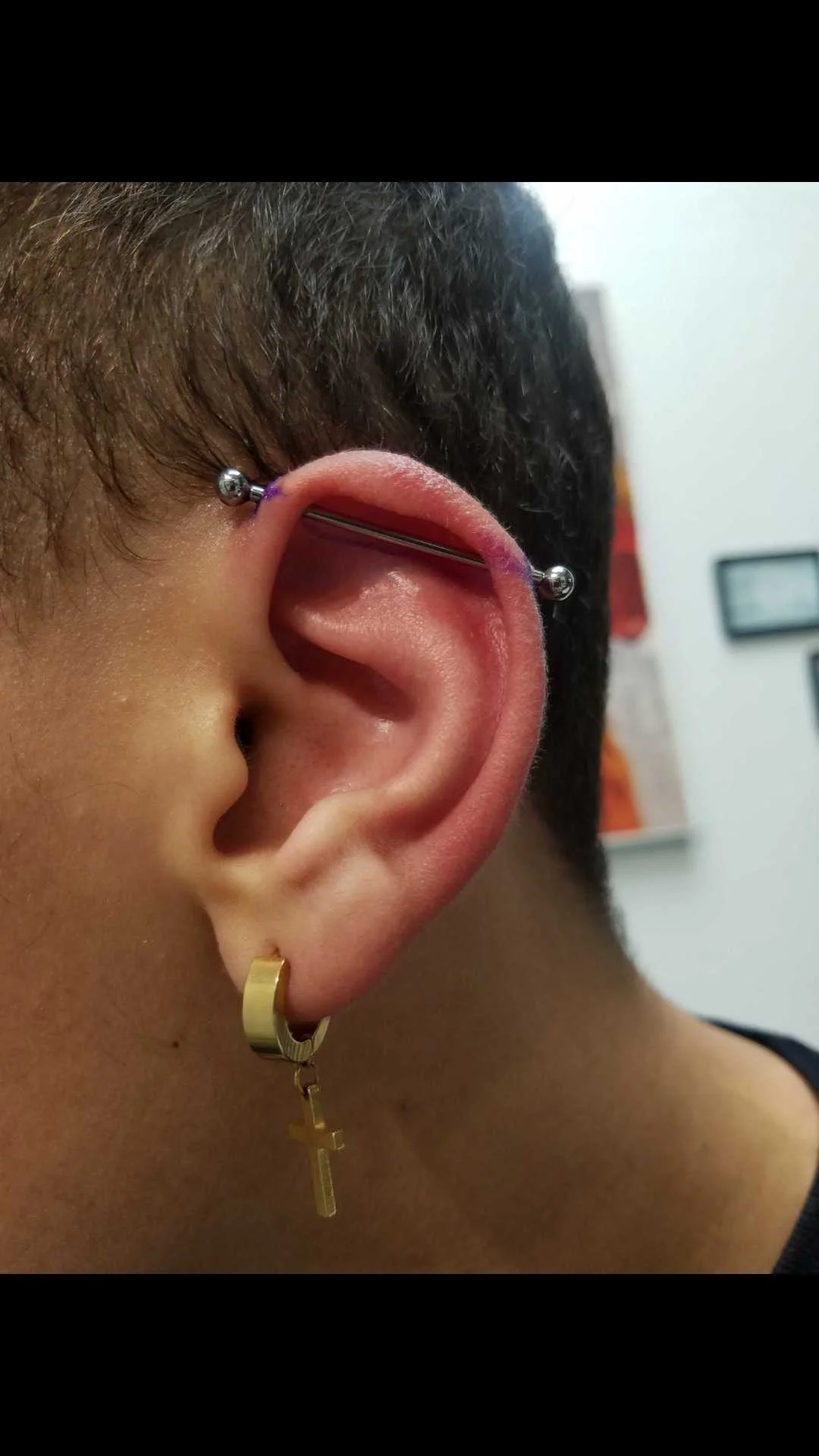 Ear with industrial barbell piercing and gold hoop earring with cross charm