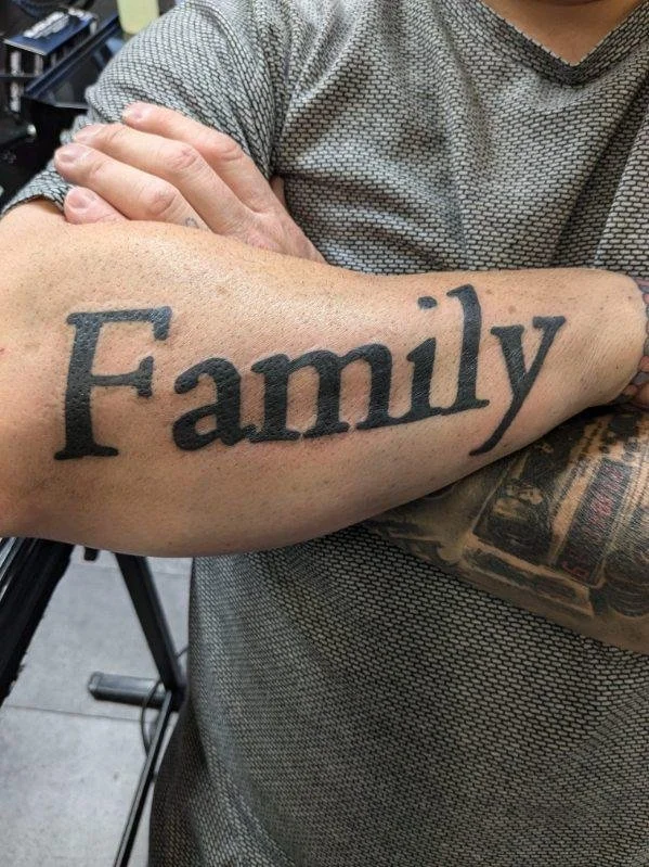 Tattoo of the word 'Family' in large black letters on a person's arm.