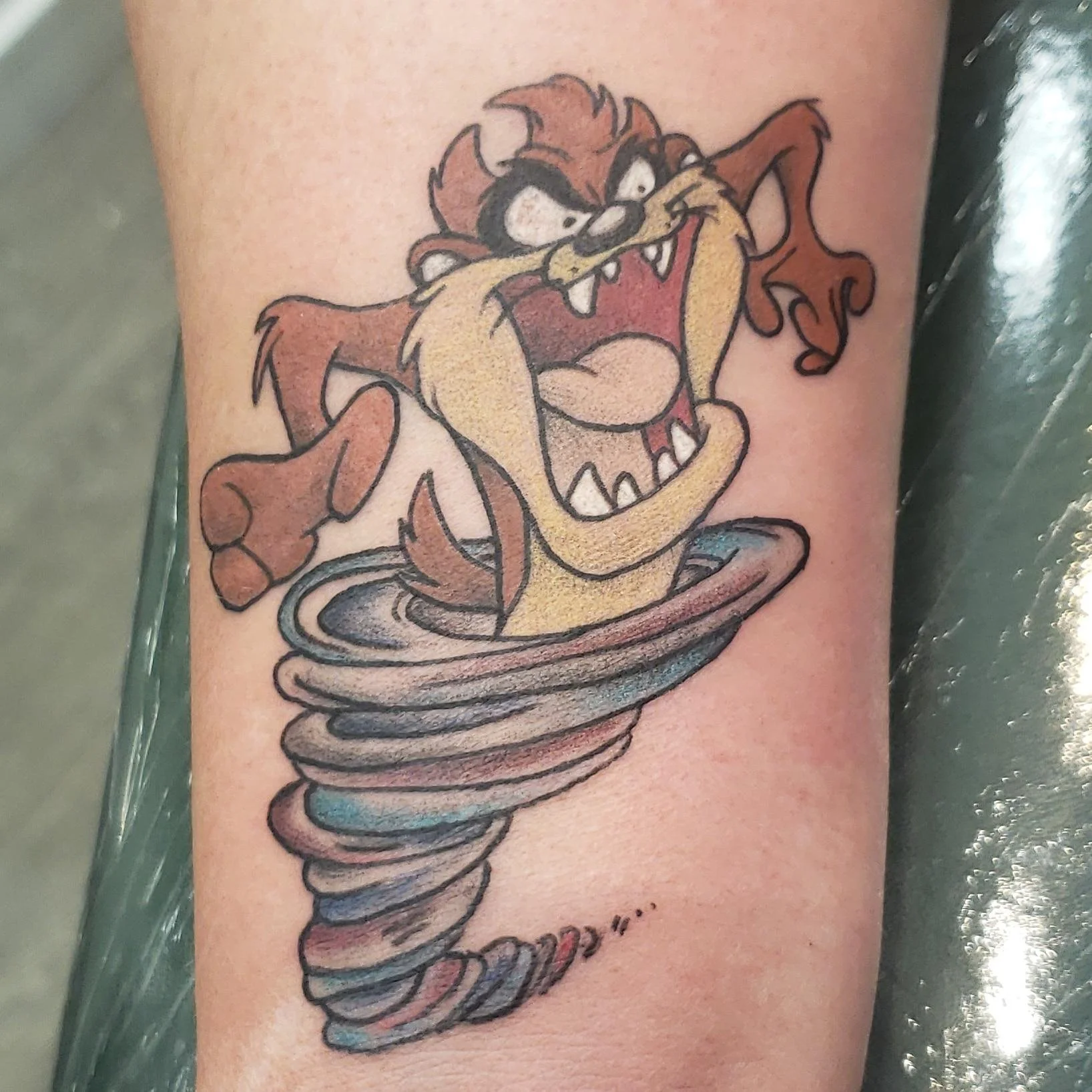 Tattoo of a cartoon Tasmanian Devil character spinning in a cyclone on human skin.