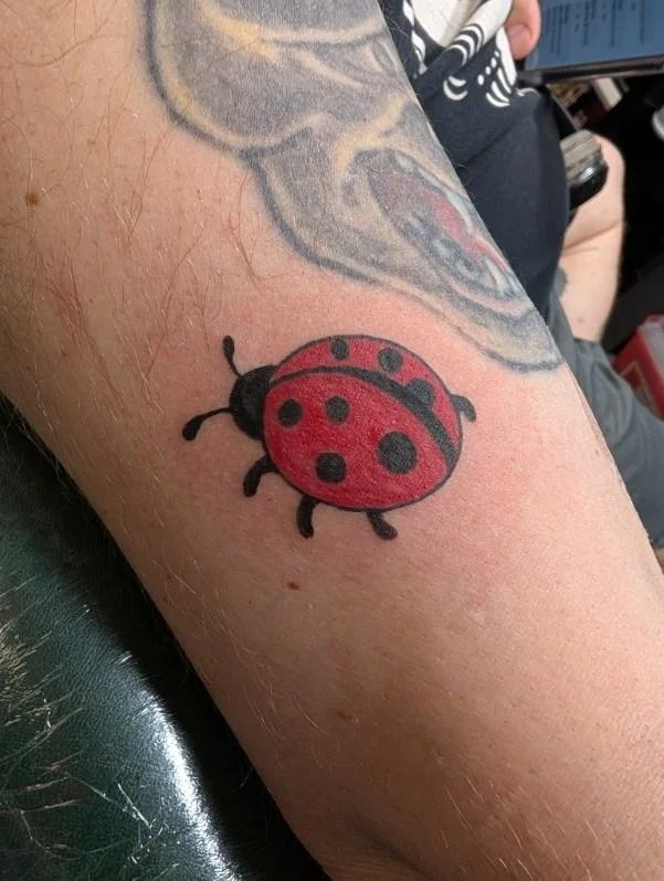 Tattoo of a red ladybug with black spots on a person's arm.
