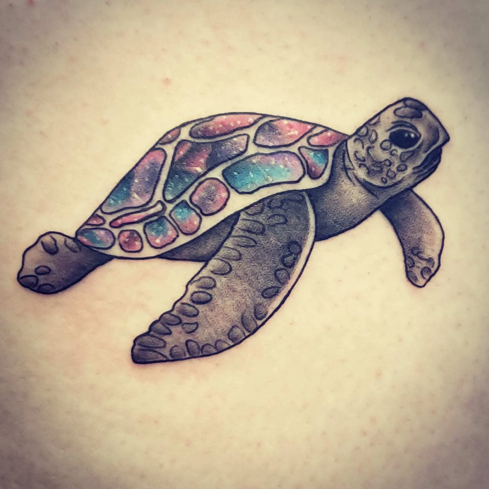 Colorful turtle tattoo on skin, featuring detailed flippers and a shell with a galaxy-like pattern in shades of pink, purple, and blue.