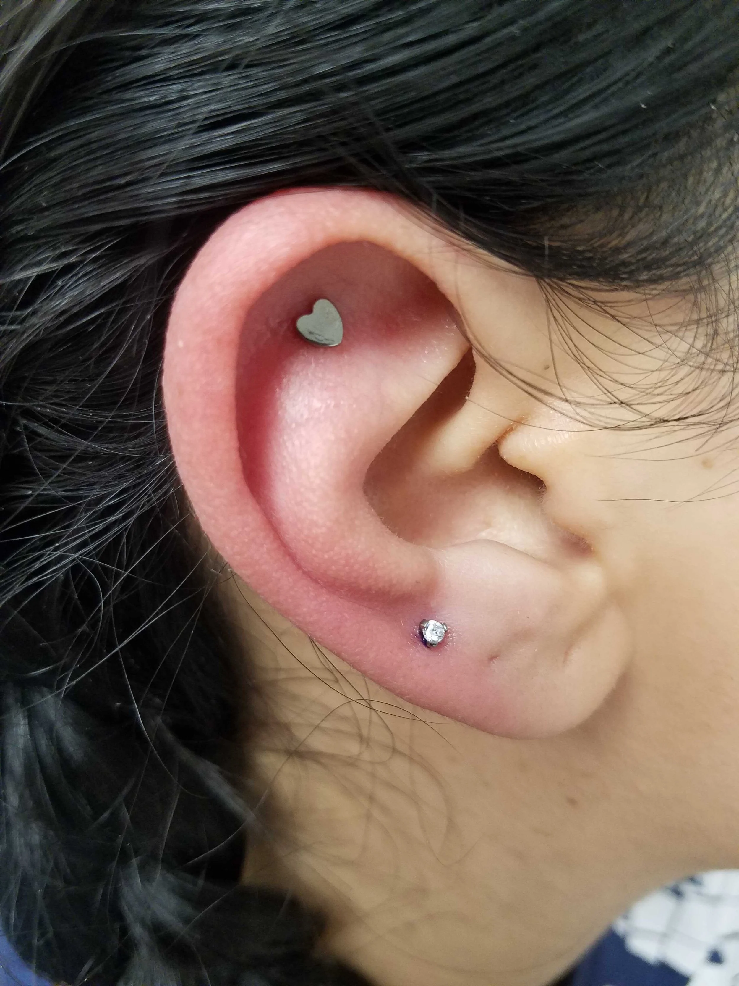 Close-up of an ear with a heart-shaped helix piercing and a small diamond stud in the earlobe.