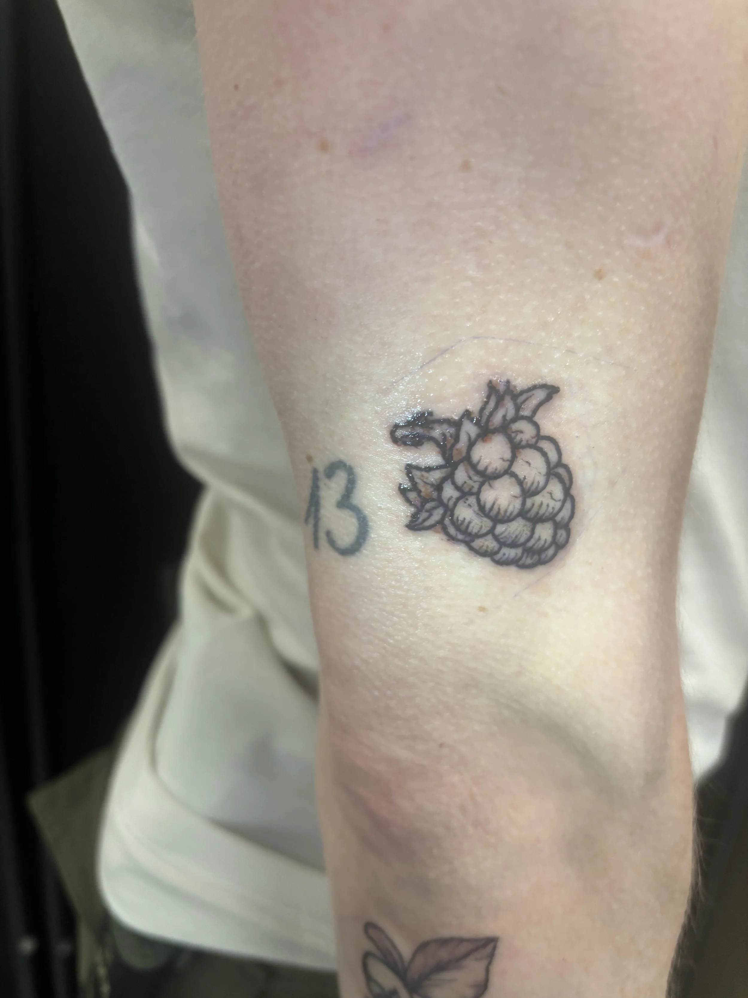 Tattoo of a cluster of berries with leaves and the number 13 on a person's arm.